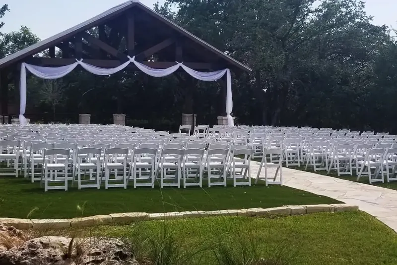 Outdoor wedding ceremony with rows of white folding chairs and a white-draped pavilion altar