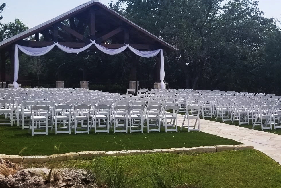 Outdoor wedding ceremony with rows of white folding chairs and a white-draped pavilion altar