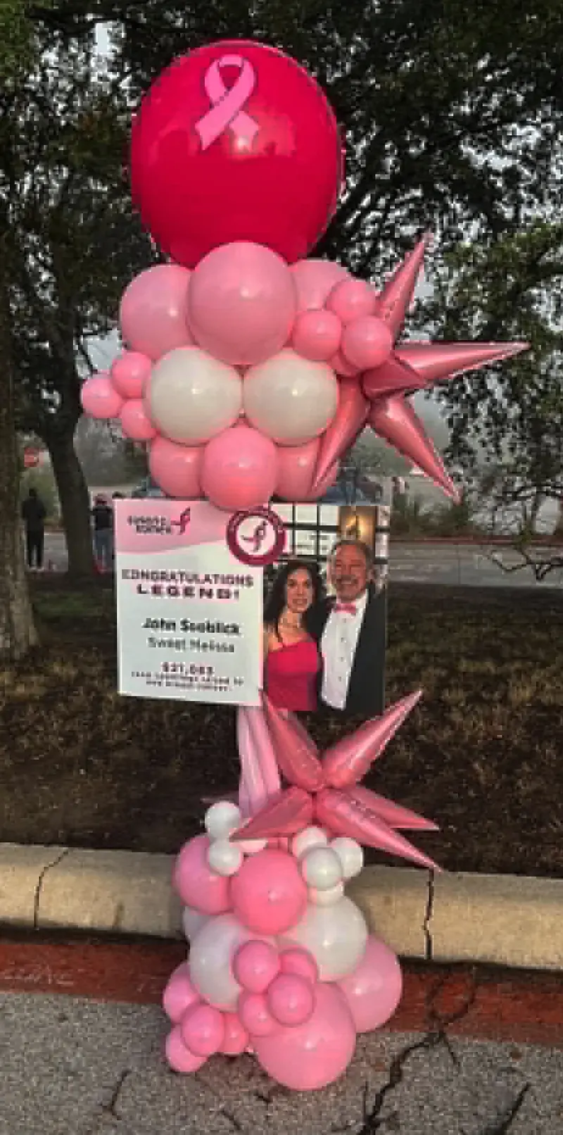 Breast cancer awareness balloon column in pink and white with ribbon balloon, pink star foils, and 'Legend' tribute sign