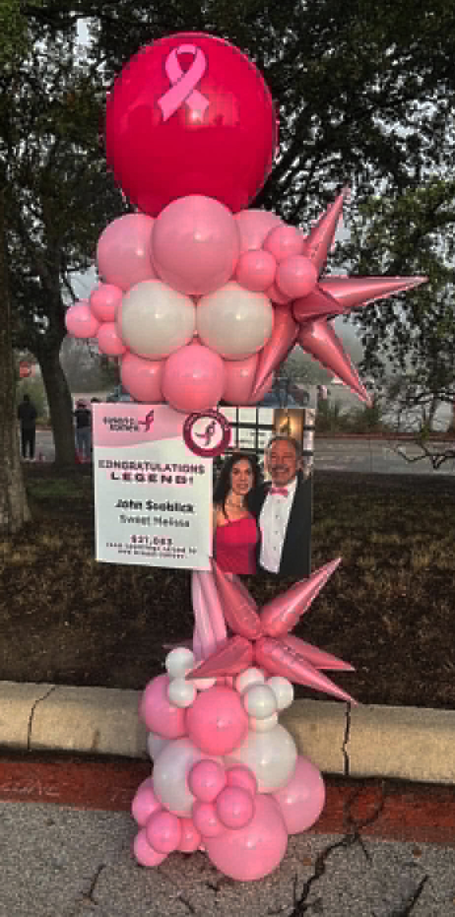Breast cancer awareness balloon column in pink and white with ribbon balloon, pink star foils, and 'Legend' tribute sign
