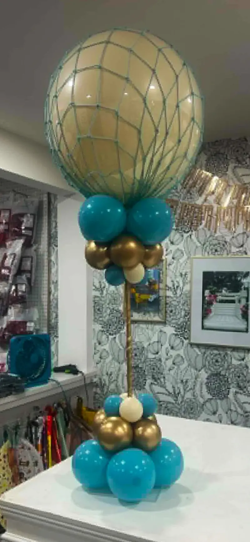 Custom hot air balloon centerpiece — cream sphere in teal netted basket on gold pole with teal, gold, and cream balloon base