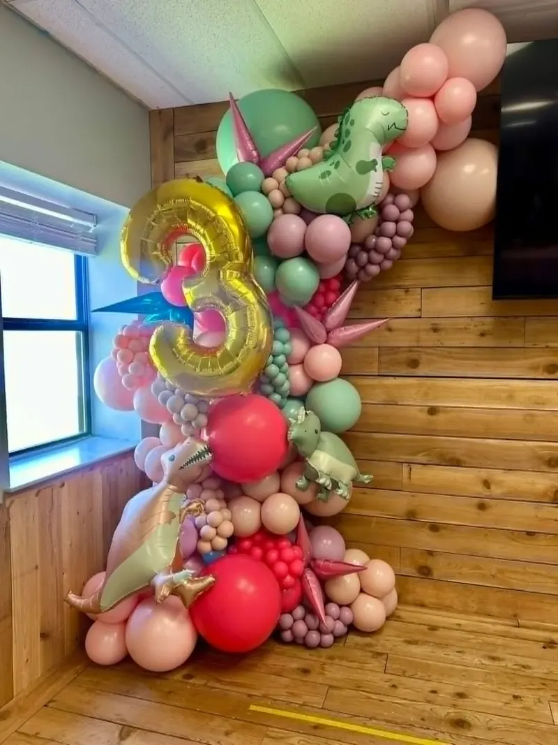 Dinosaur 3rd birthday balloon garland with gold number 3 foil, green and pink dinosaur foils, sage, pink, mauve, and red balloons with spike accents