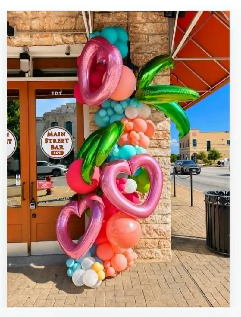 Main Street Bar storefront balloon garland with pink heart foils, green tropical leaf foils, and coral, teal, and pink organic balloons