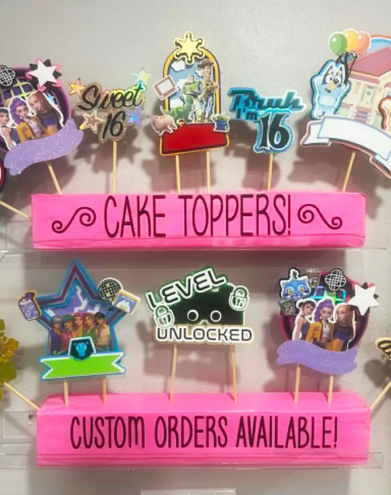 Custom cake toppers display featuring Sweet 16, Toy Story, Bluey, Level Unlocked, and other personalized designs with Custom Orders Available sign