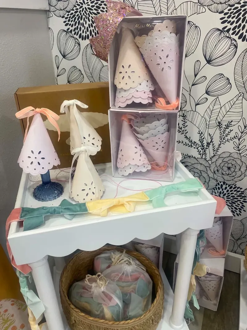Meri Meri scalloped pink and white party hats with peach ribbons on a display tray
