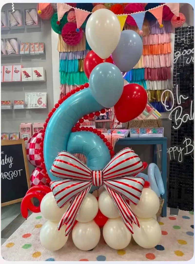 Candy cane themed 6th birthday balloon stack with teal number 6, red and white striped bow foil, and cream balloon base