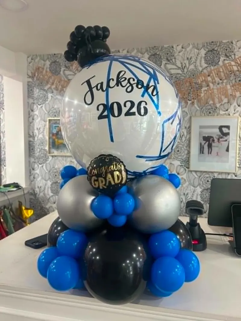 Personalized Jackson 2026 graduation balloon stack with custom-painted clear orb, Congrats Grad foil, and royal blue, silver, and black base