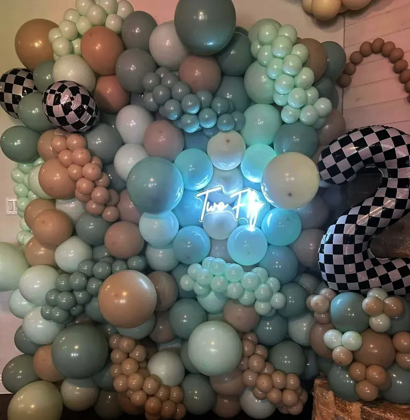 Organic balloon wall in sage, mint, dusty tan, and white with checkered foil accents and 'Two Fly' neon sign